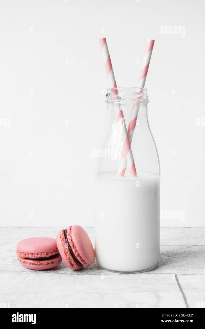Piccola bottiglia di latte in vetro con cannucce di carta a strisce di caramelle rosa e macaron rosa Foto Stock