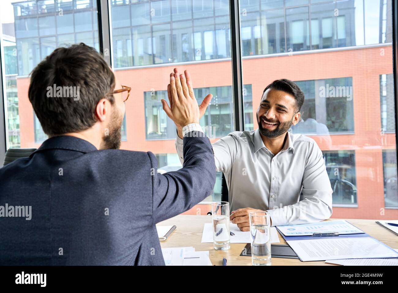 Due uomini d'affari professionali felici e diversi che danno cinque in alto durante la riunione. Foto Stock