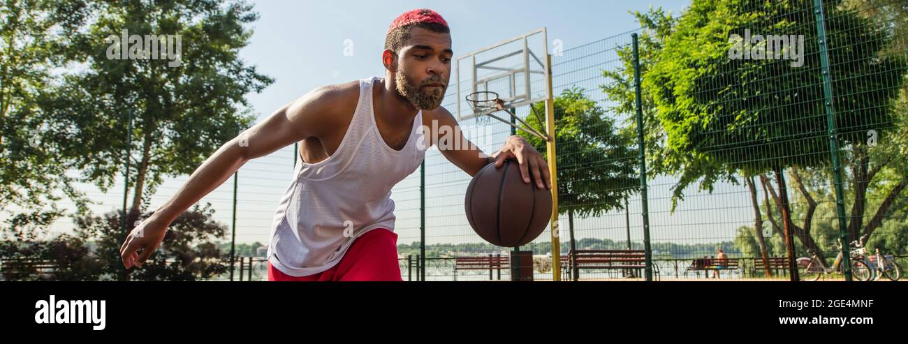 Giovane uomo afroamericano che gioca a basket all'aperto, banner Foto Stock