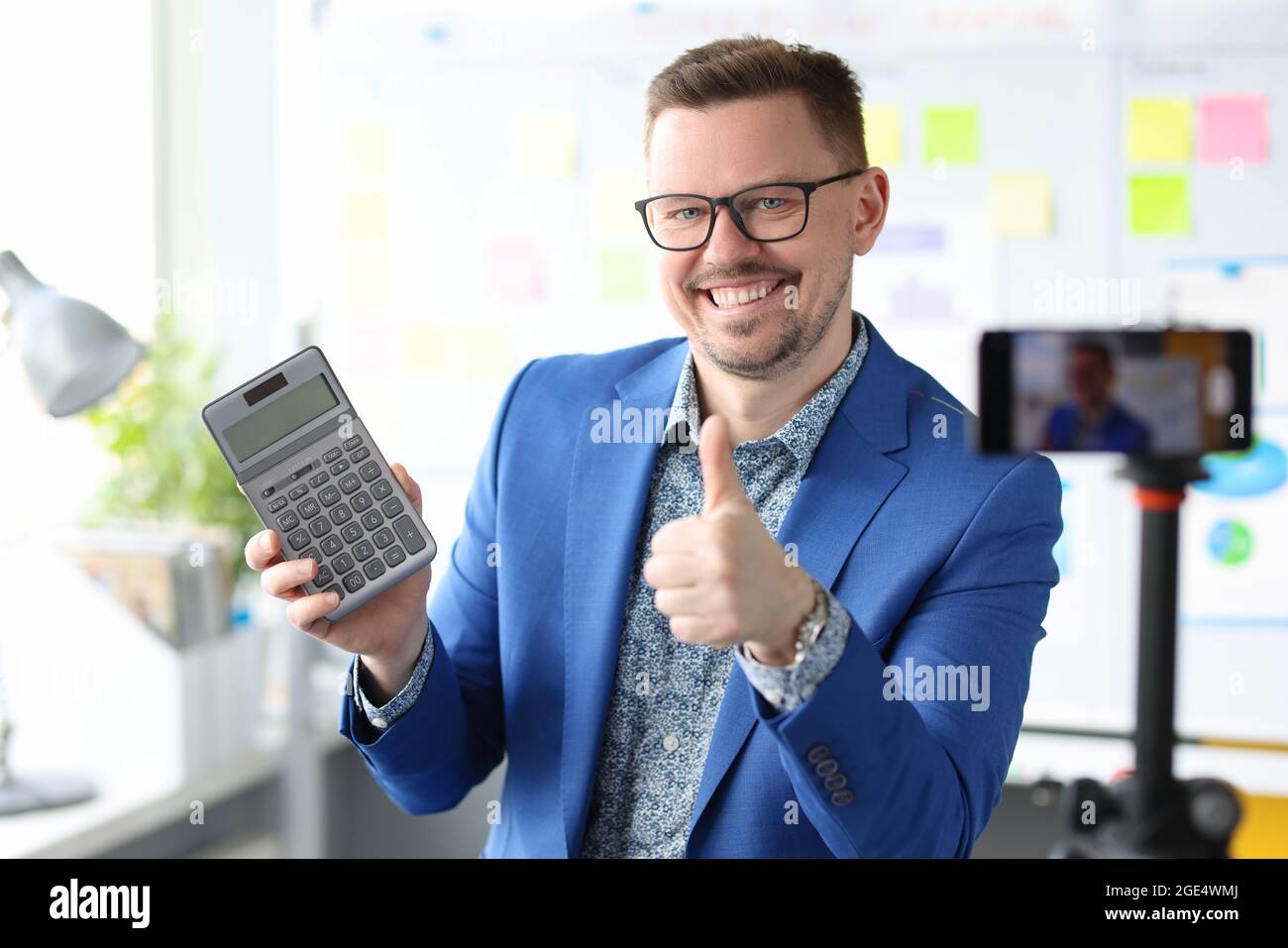 Un uomo d'affari blogger sorridente tiene una calcolatrice e registra video di formazione sui guadagni Foto Stock