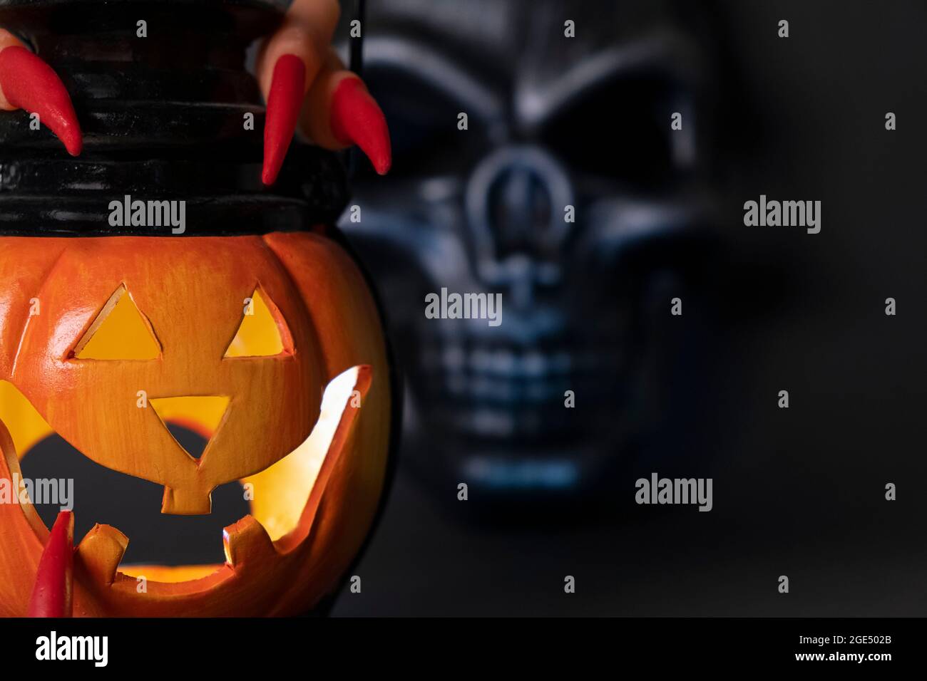 Sfondo di Halloween. Zucca incandescente e cranio nero su sfondo scuro. Dita umane con lunghi artigli rossi Foto Stock