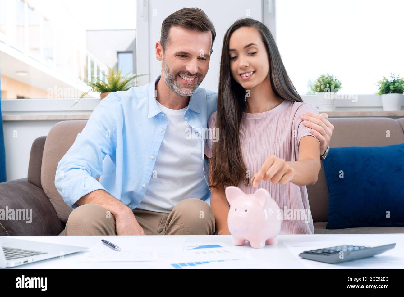 Mano che mette la moneta alla banca del piggy. La giovane coppia sta risparmiando i soldi per la loro nuova sede. Foto Stock