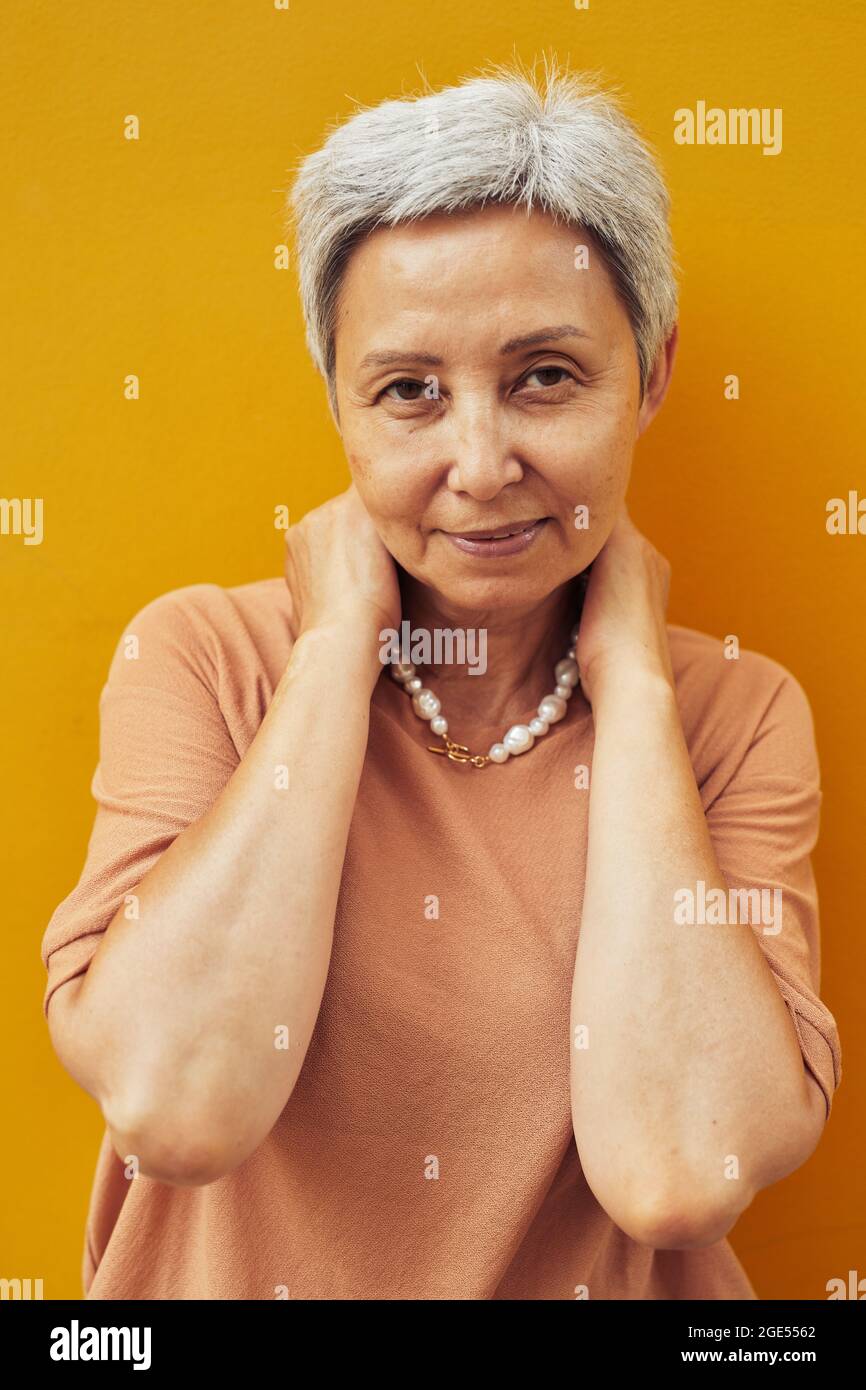 Ritratto verticale di donna matura sicura sorridente all'aperto mentre si posa su sfondo giallo e guardando la fotocamera, copia spazio Foto Stock