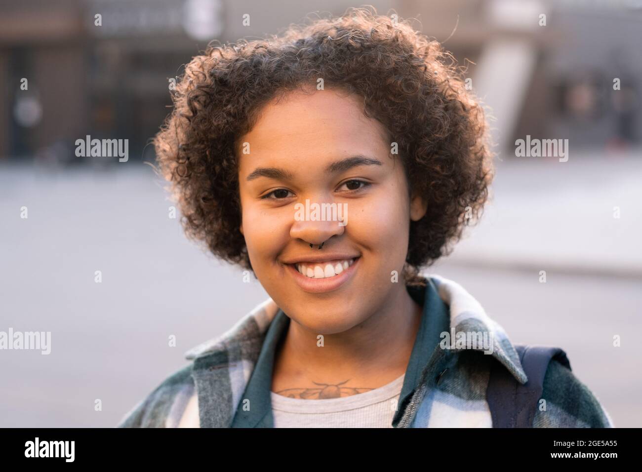 Felice ragazza di etnia africana in piedi davanti alla macchina fotografica in ambiente urbano Foto Stock