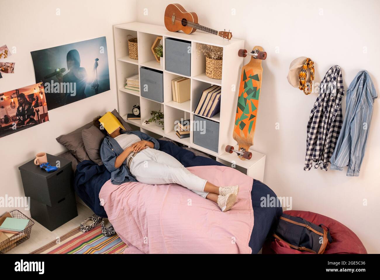 Ragazza adolescente con libro aperto sulla sua faccia che pappano a letto da scaffale con libri Foto Stock