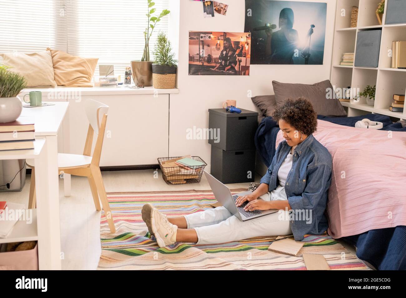 Grazioso studente adolescente con computer portatile che esegue il test online mentre si siede a letto sul pavimento Foto Stock
