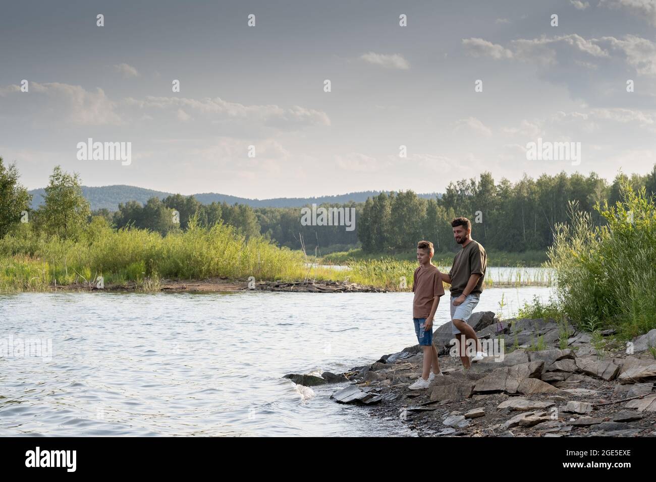 Padre e figlio si levano in piedi vicino al lago mentre godendo la vacanza estiva nel paese Foto Stock