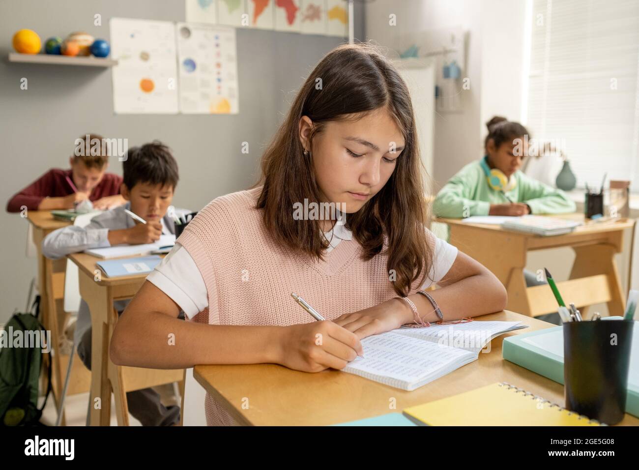 Studentessa elementare caucasica che prende appunti mentre si siede alla scrivania durante la lezione Foto Stock