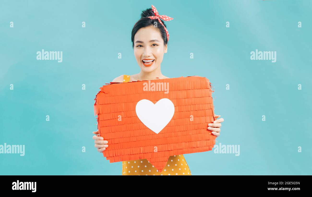 Attraente donna che tiene il simbolo del cuore di come e amore icona di notifica dei social media felice con i seguaci e i fan su Internet. Foto Stock