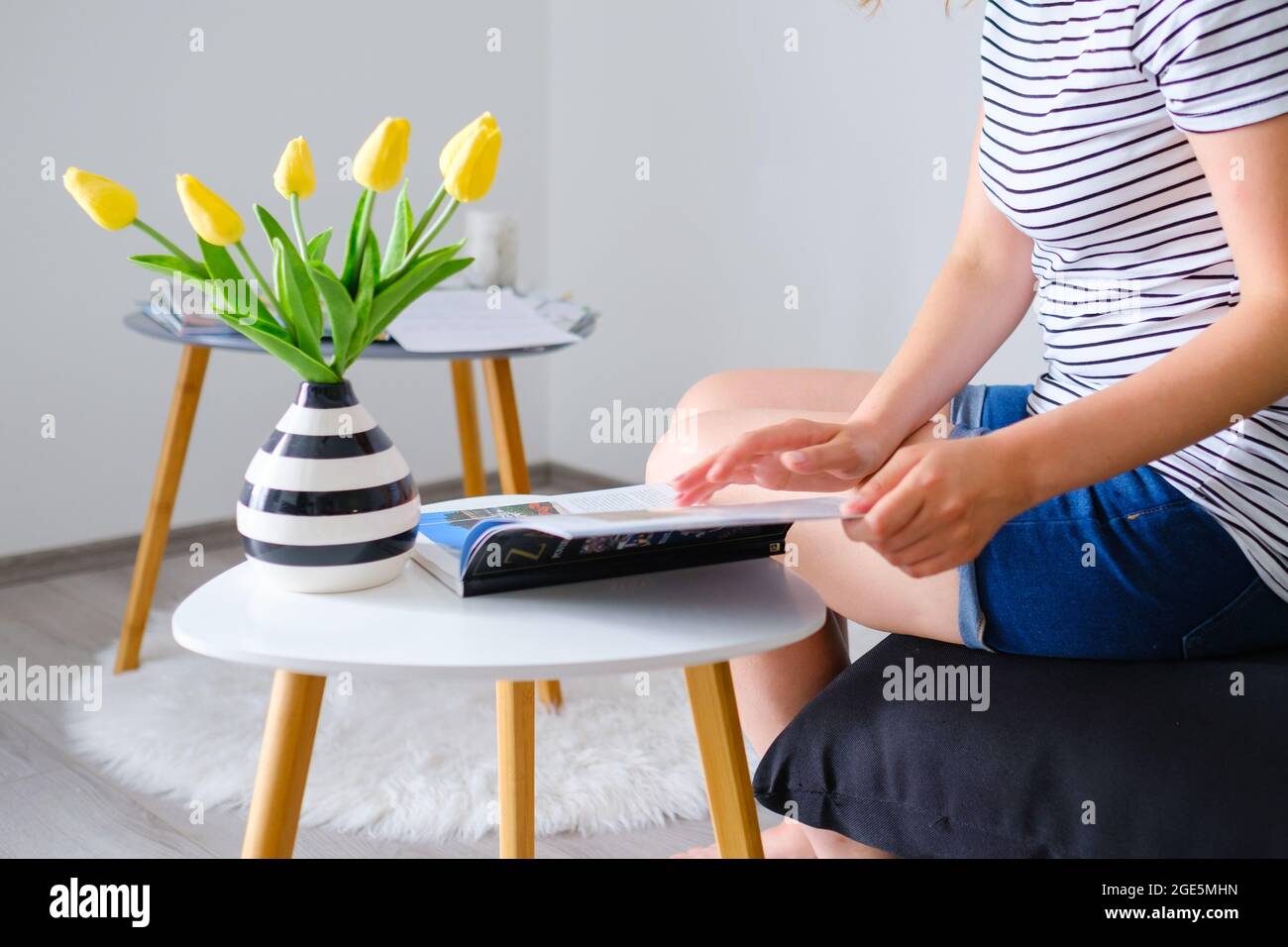 Giovane donna che legge un catalogo o una rivista di viaggio e sceglie una destinazione per il viaggio in un bellissimo soggiorno moderno Foto Stock