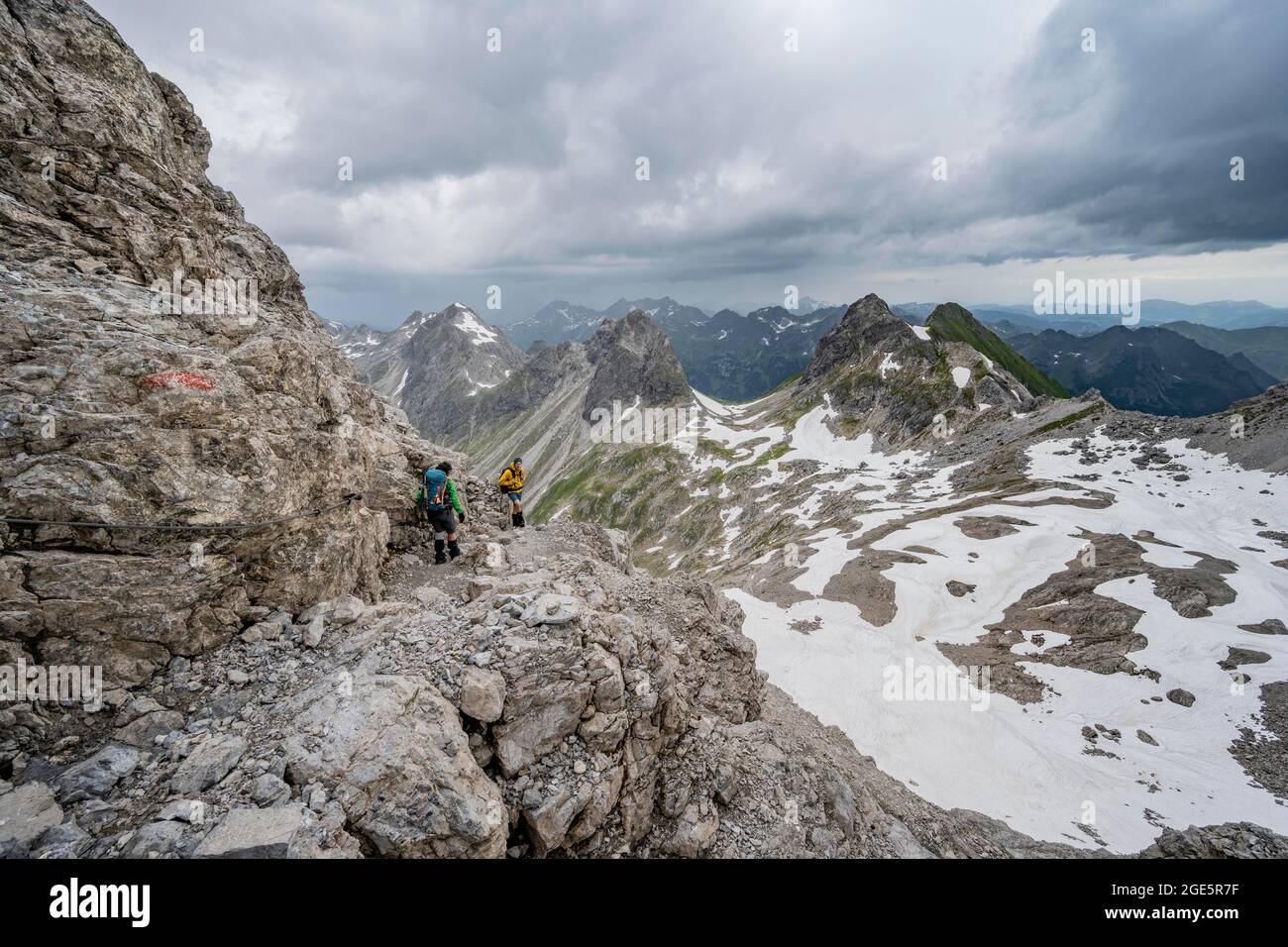 Escursionista e escursionista discesa terreno roccioso, sullo sfondo panorama montano con vecchi campi di neve e cime rocciose di montagna, Heilbronner Weg, Allgaeu Foto Stock