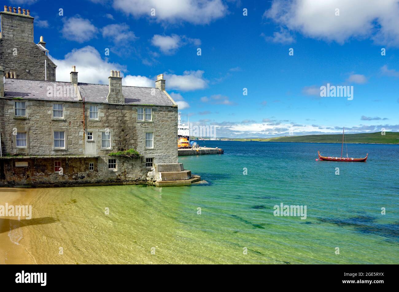 Baia tranquilla con acqua cristallina, porto, casa di pietra e nave vichinga, Lerwick, Isole Shetland, Scozia, Regno Unito Foto Stock