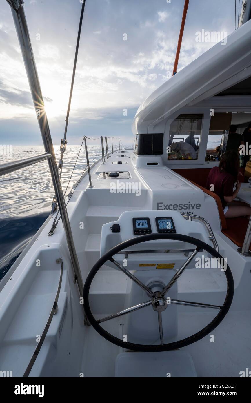 Volante in cabina di pilotaggio sul ponte di un catamarano a vela nella luce della sera, stella del sole, gita in barca a vela, Dodecanese, Grecia Foto Stock