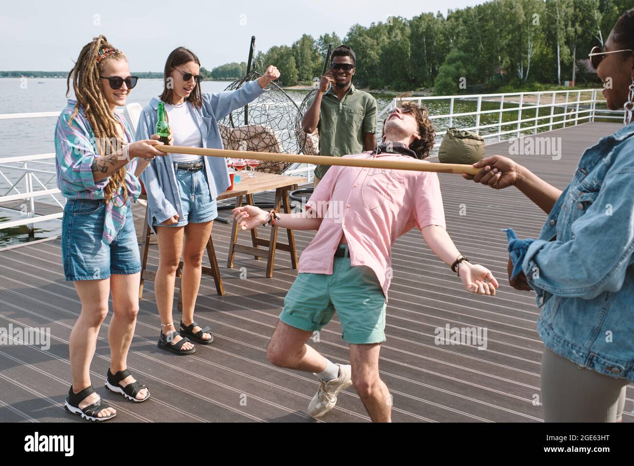 Gruppo di giovani riuniti sul molo di legno per fare una festa e giocare a limbo game Foto Stock