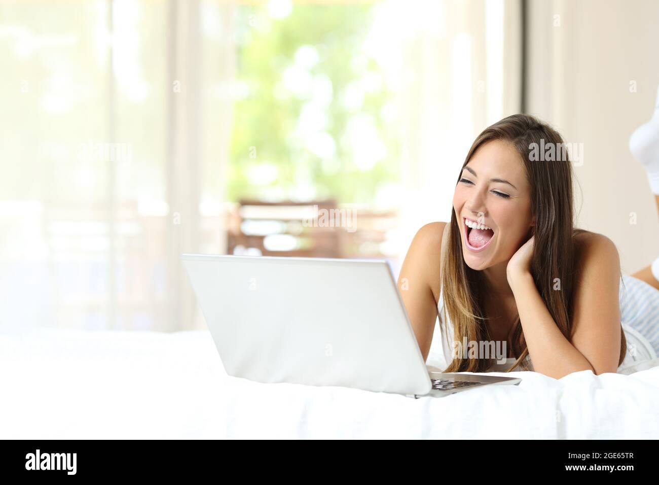 Donna felice che guarda i video online su un computer portatile sdraiato su un letto a casa Foto Stock