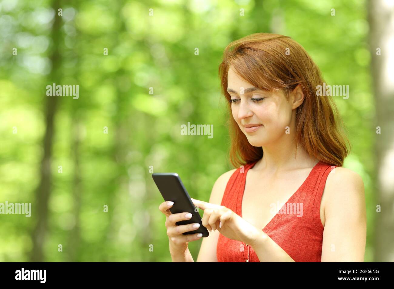Donna soddisfatta che controlla lo smartphone camminando in un parco verde Foto Stock