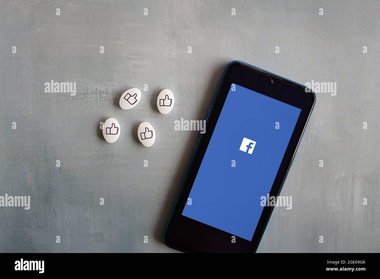 Concetto di dipendenza dai social media. Il logo Facebook sullo smartphone e l'icona dei pollici sulla capsula bianca delle pillole. Foto Stock