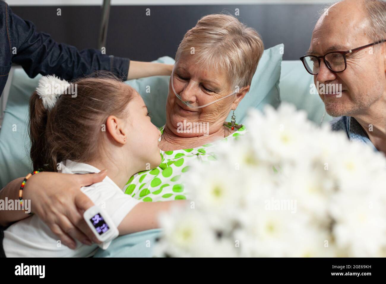 Piccola nipote che porta fiori durante la visita della nonna malata supportandola dopo l'intervento medico durante la terapia medica. Bambino abbracciando malato paziente anziano in visita nel reparto ospedaliero Foto Stock