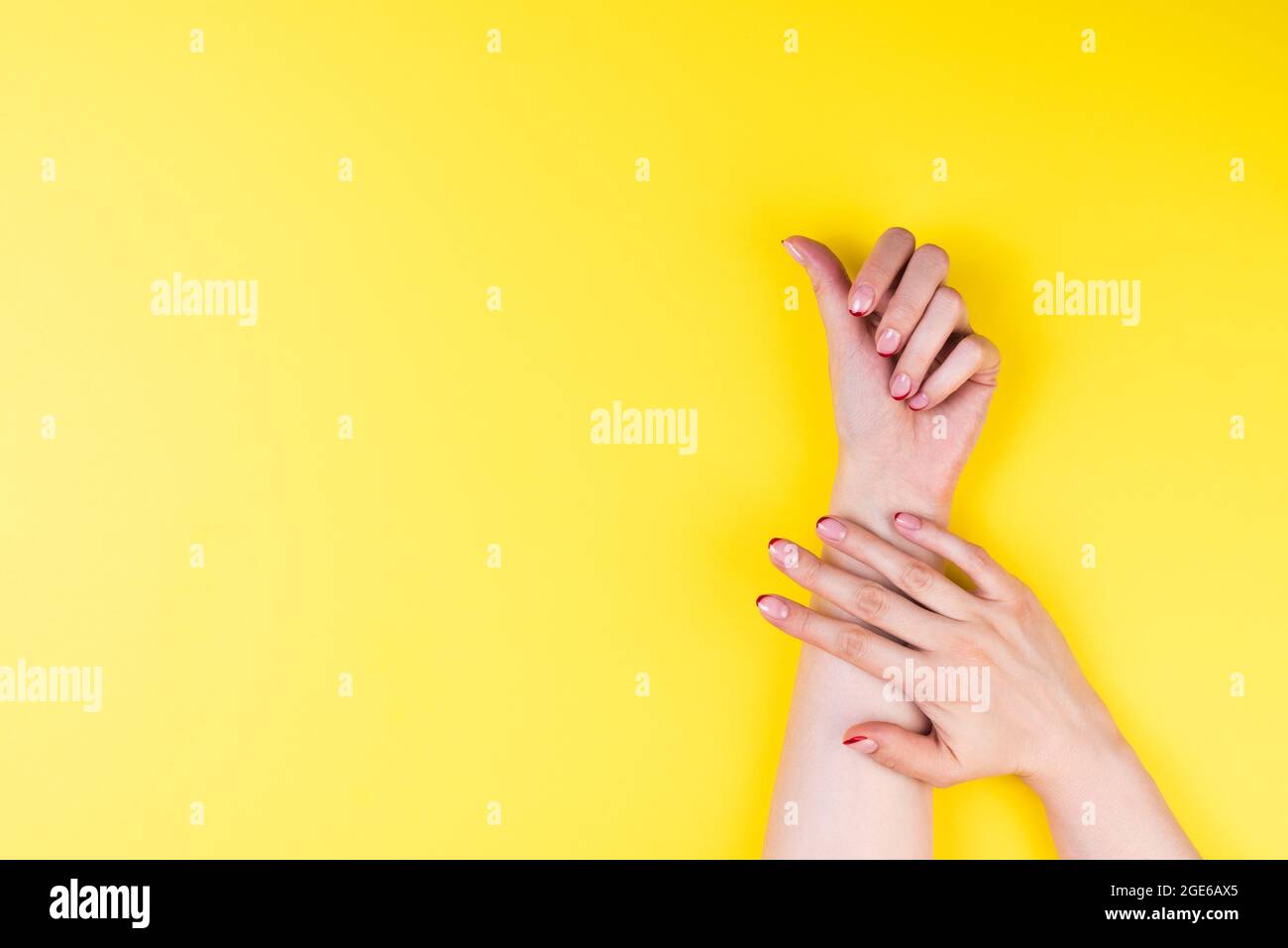 Mani femminili con una manicure francese d'autunno alla moda con punte rosse sul bordo libero del chiodo. Ultimat sfondo giallo Foto Stock