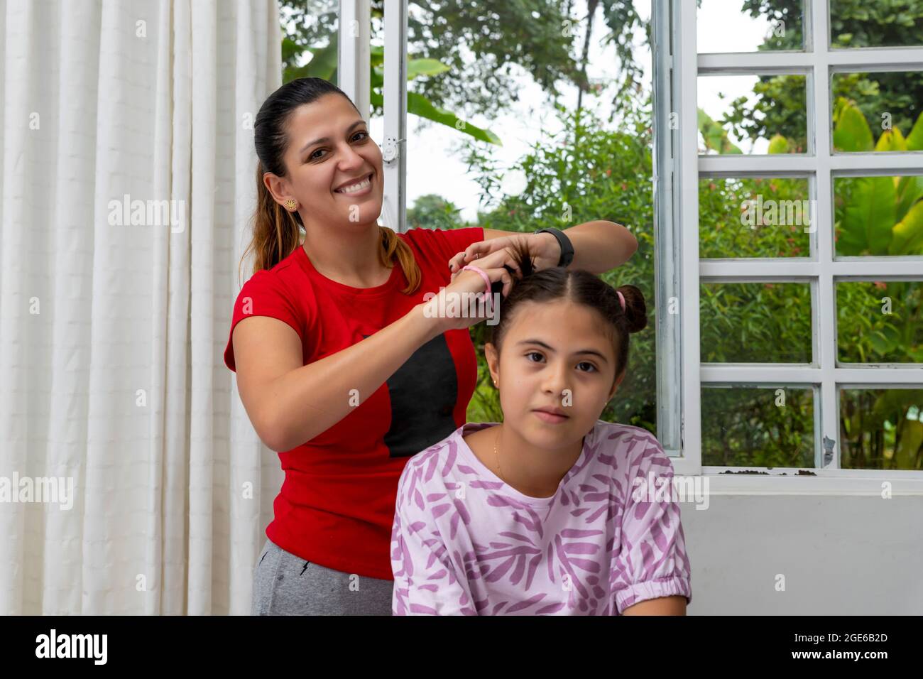 Madre Latina styling capelli di figlia e guardando la macchina fotografica Foto Stock