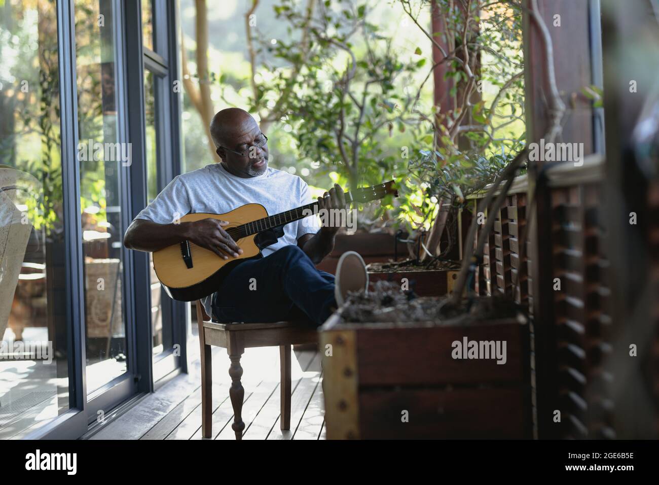 Rilassante uomo afroamericano su un balcone soleggiato che suona la chitarra Foto Stock