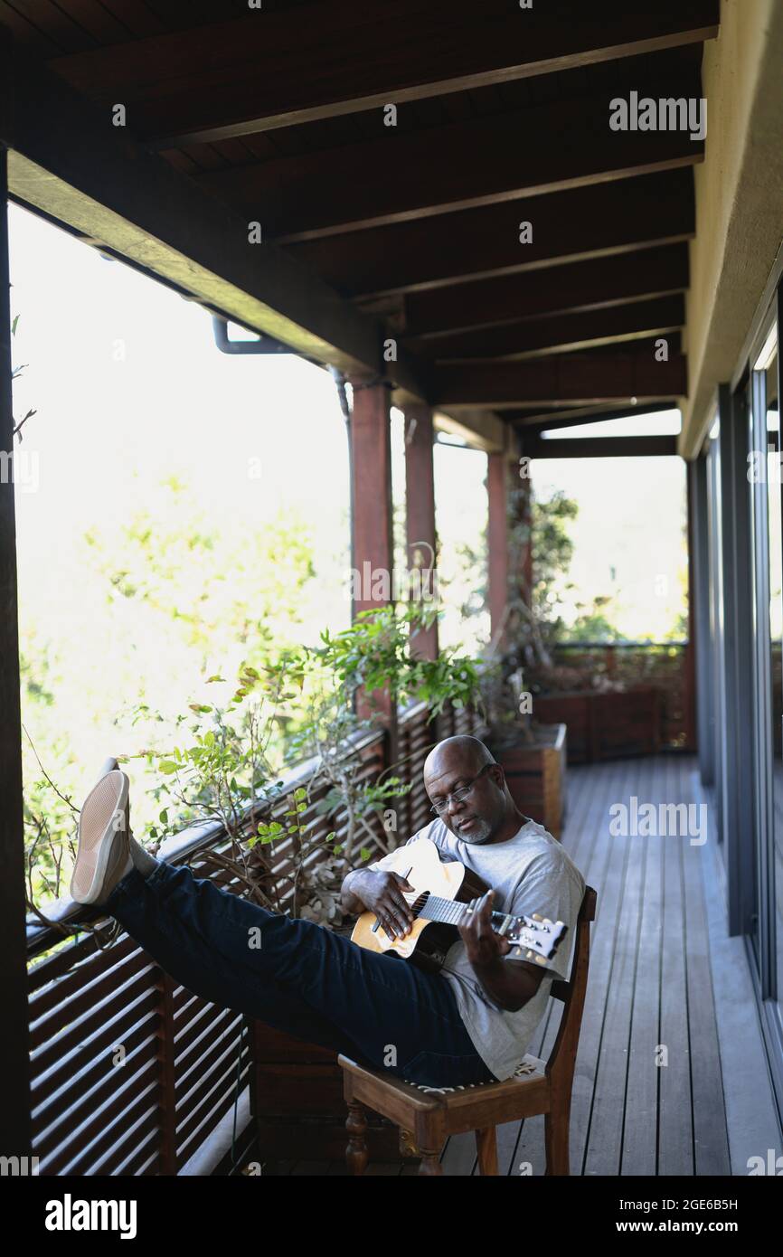 Felice uomo afroamericano senior sul balcone soleggiato che suona la chitarra Foto Stock