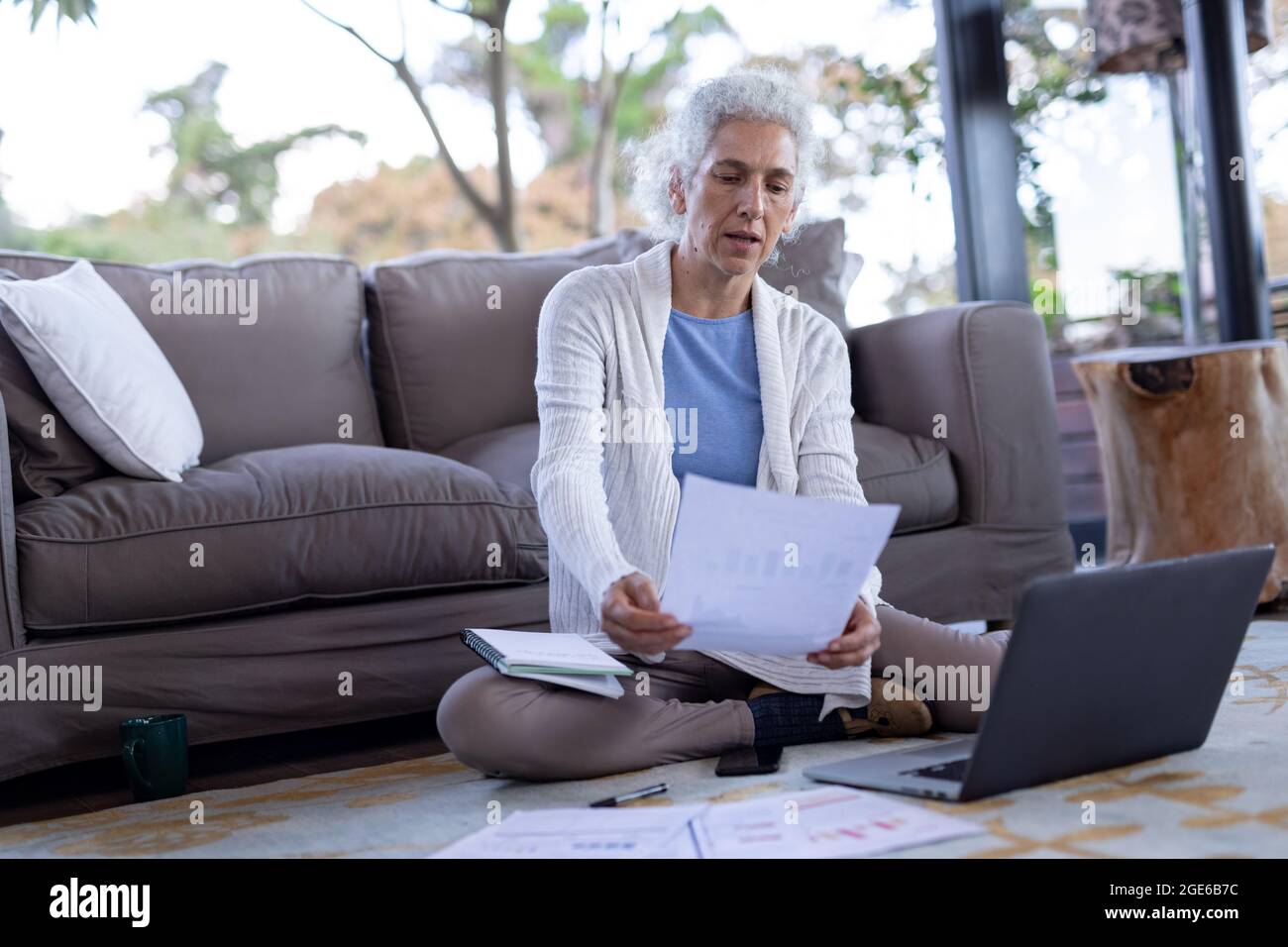 Donna caucasica anziana in soggiorno seduta sul pavimento e utilizzando un computer portatile Foto Stock