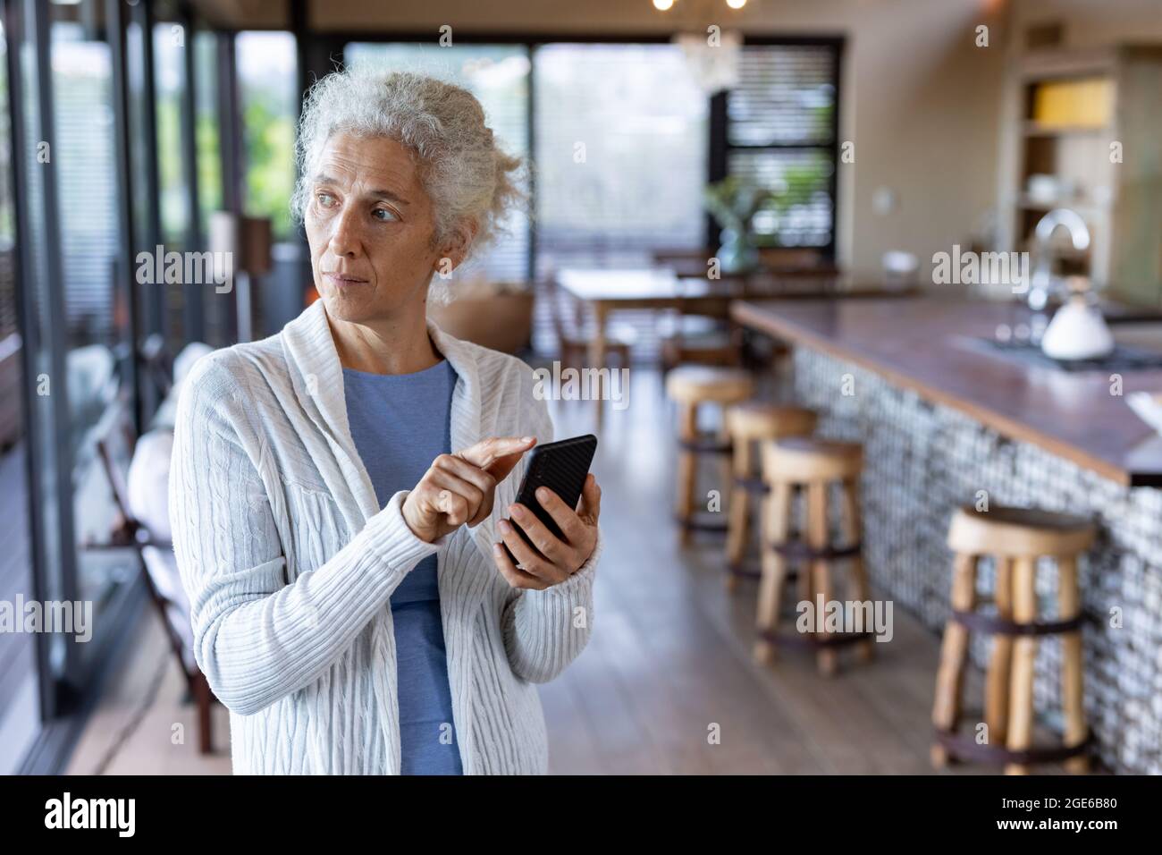 Donna caucasica anziana in cucina in piedi e utilizzando smartphone Foto Stock