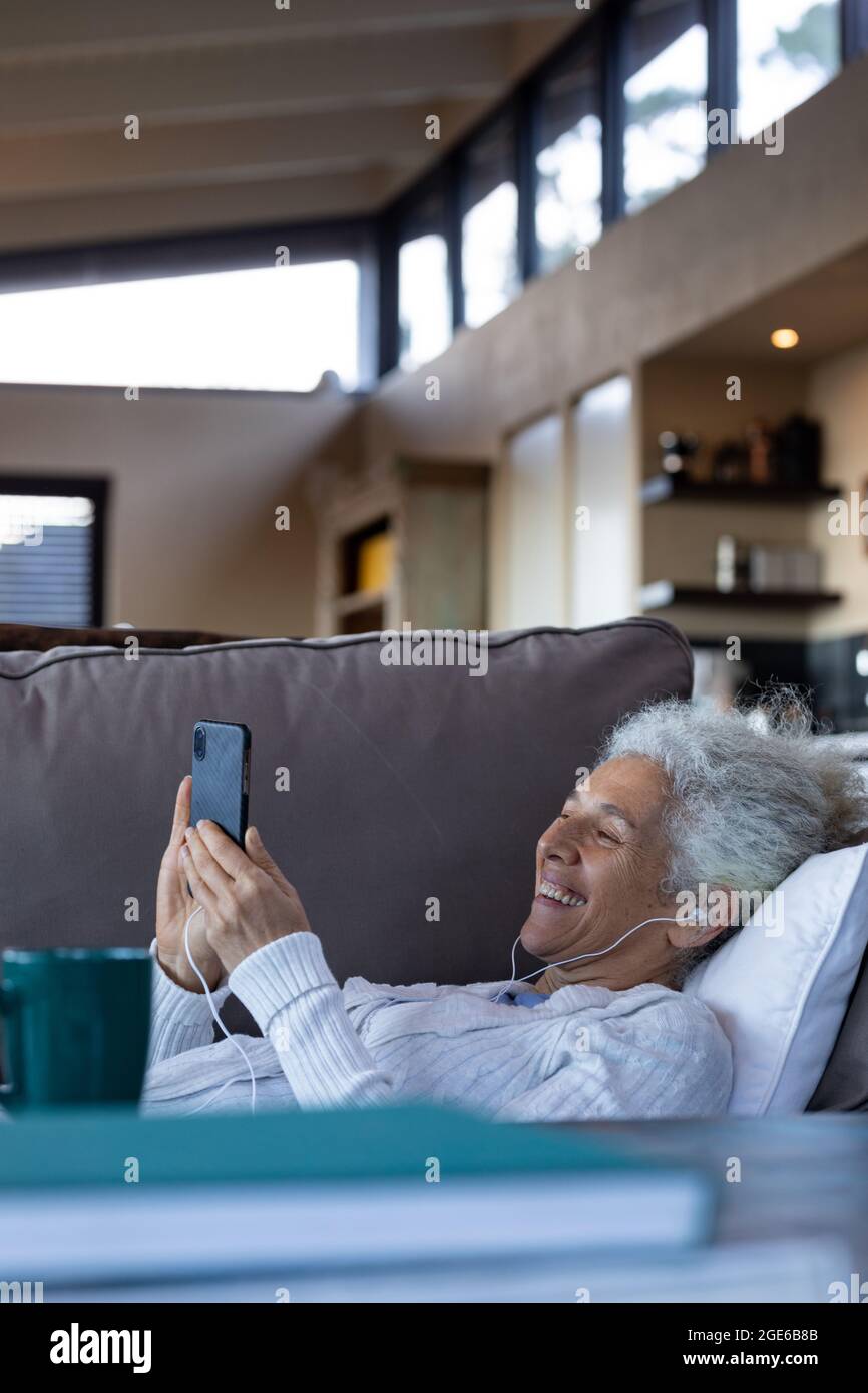 Felice anziana donna caucasica che posa e utilizza smartphone nel soggiorno moderno Foto Stock