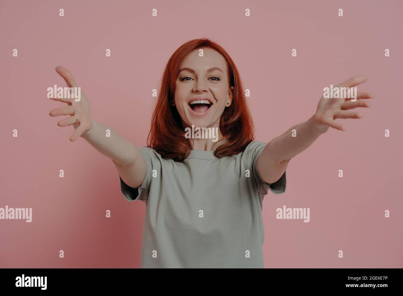 Amichevole felice zenzero donna allungare le braccia per abbraccio e sorridente allegro, isolato su rosa Foto Stock