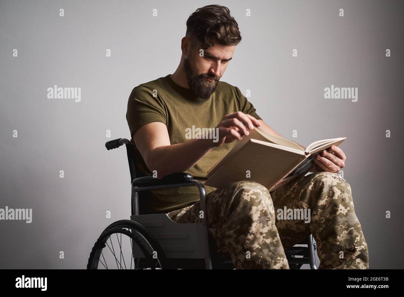 Uomo militare seduto su una sedia a rotelle e guardando le foto in un album Foto Stock