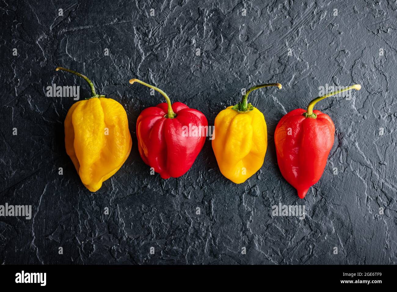 Peperoni gialli e rossi caldi jalapeno su fondo nero primo piano. Fotografia alimentare Foto Stock
