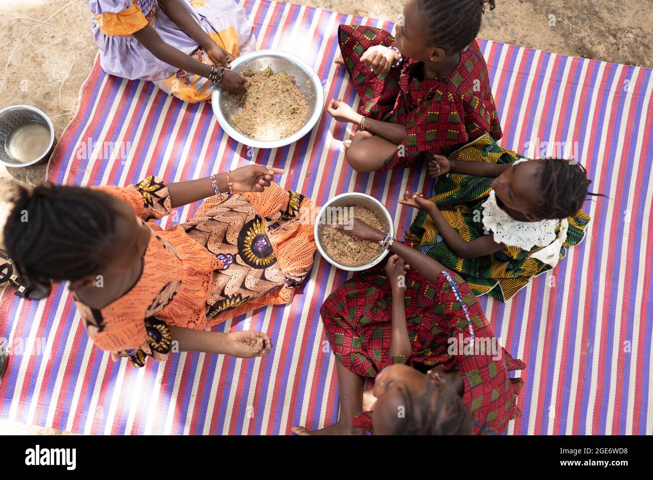 Vista dall'alto di un gruppo di ragazze africane nere ben vestite che si siedono su un tappeto a righe, godendo il loro abbondante pasto durante una celebrazione di famiglia Foto Stock