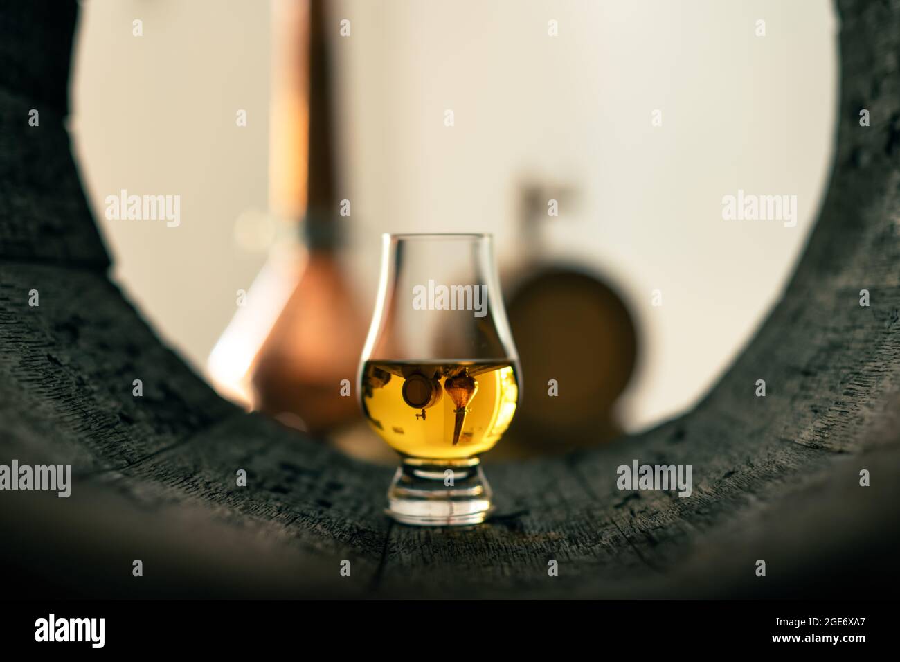 Un bicchiere di whisky in un vecchio barile di quercia. Rame alambic sullo sfondo. Tradizionale concetto di distilleria alcolica Foto Stock