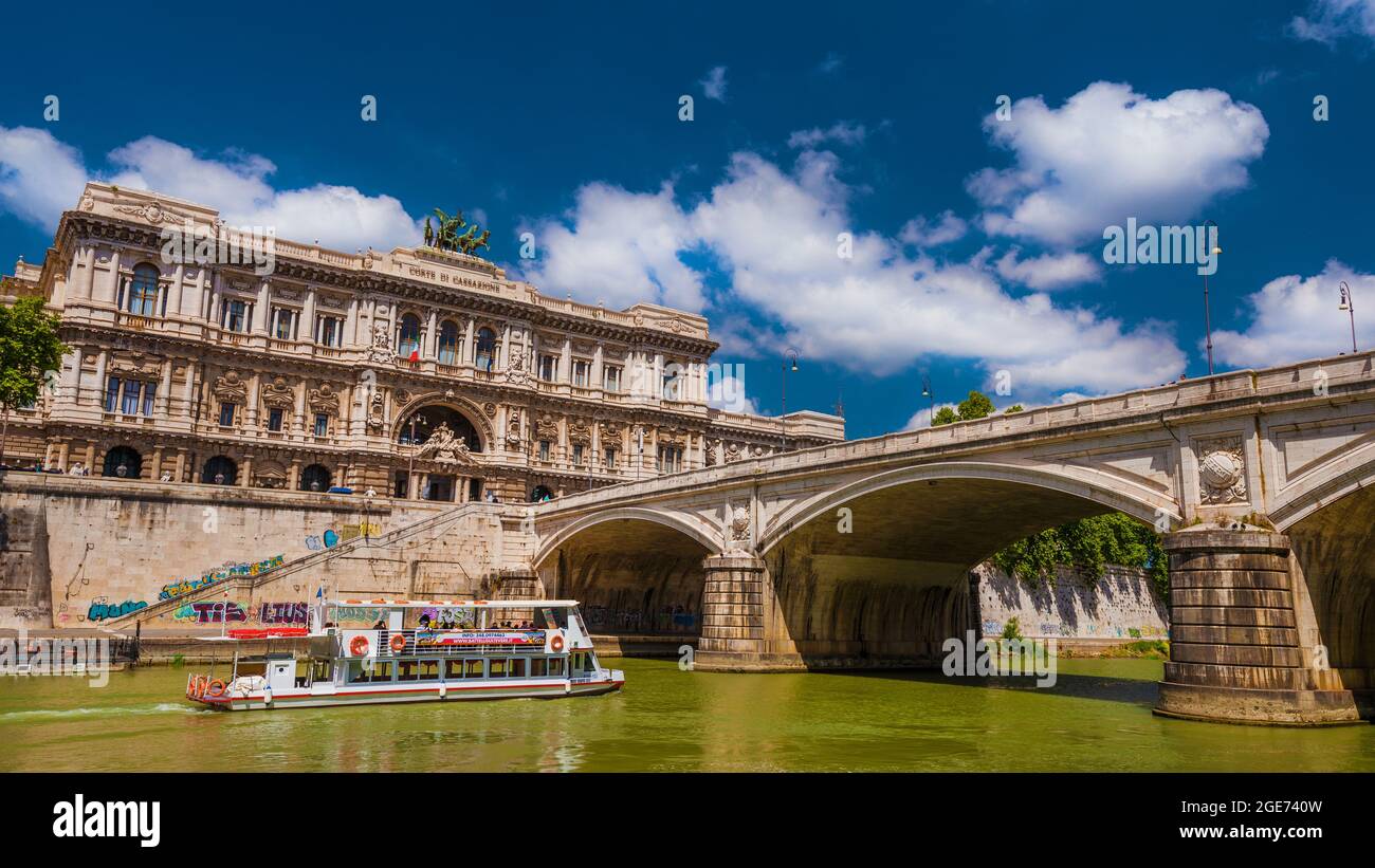 Vita e navigazione lungo il fiume Tevere. La barca turistica passa vicino al ponte Umberto i e all'antico Palazzo di Giustizia di Roma Foto Stock
