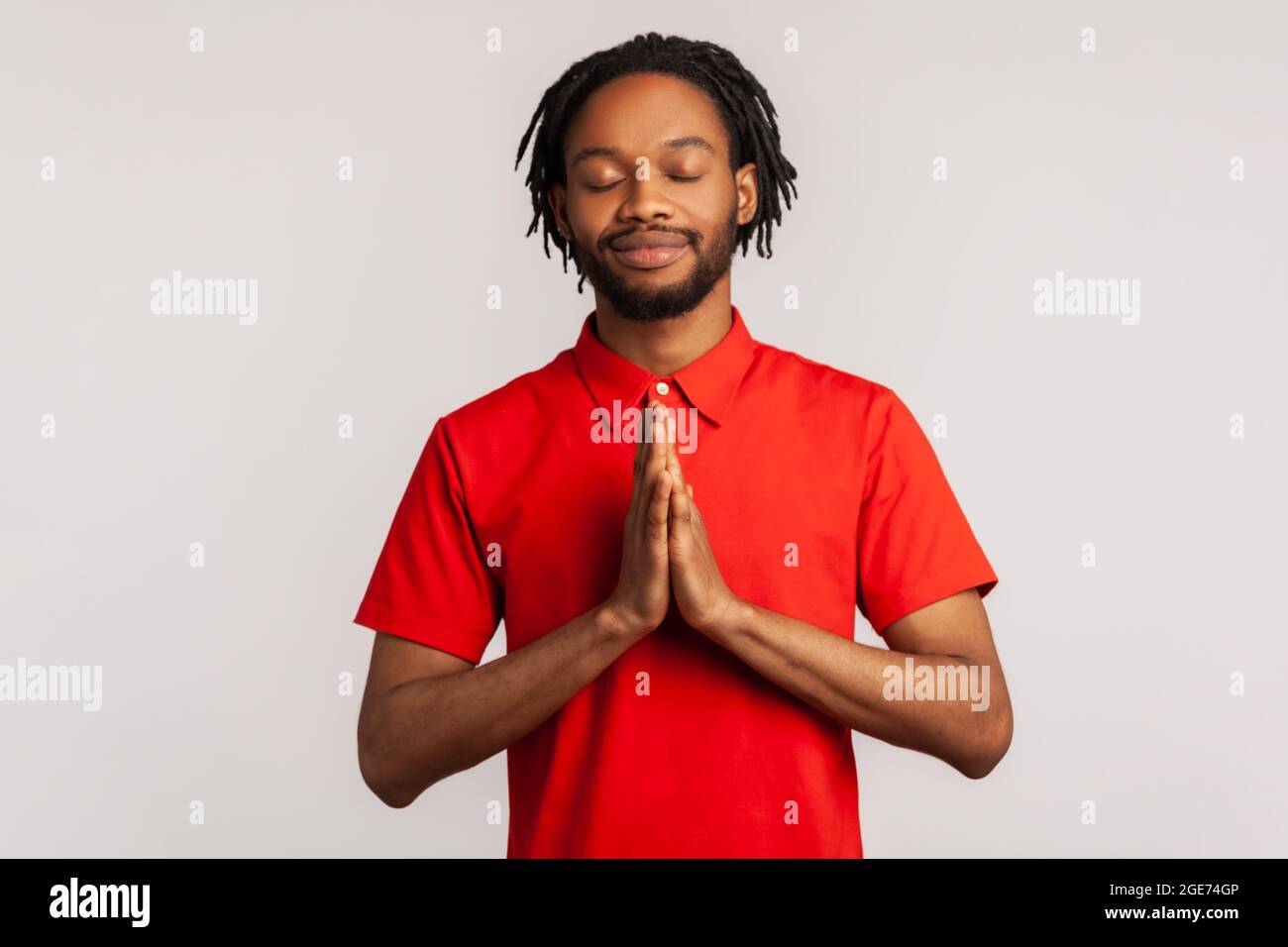 Uomo bearded che indossa una T-shirt rossa, concentrando la sua mente, mantenendo le mani movimento namaste, meditando, yoga esercizio respirazione tecnica ridurre lo stress. Indo Foto Stock