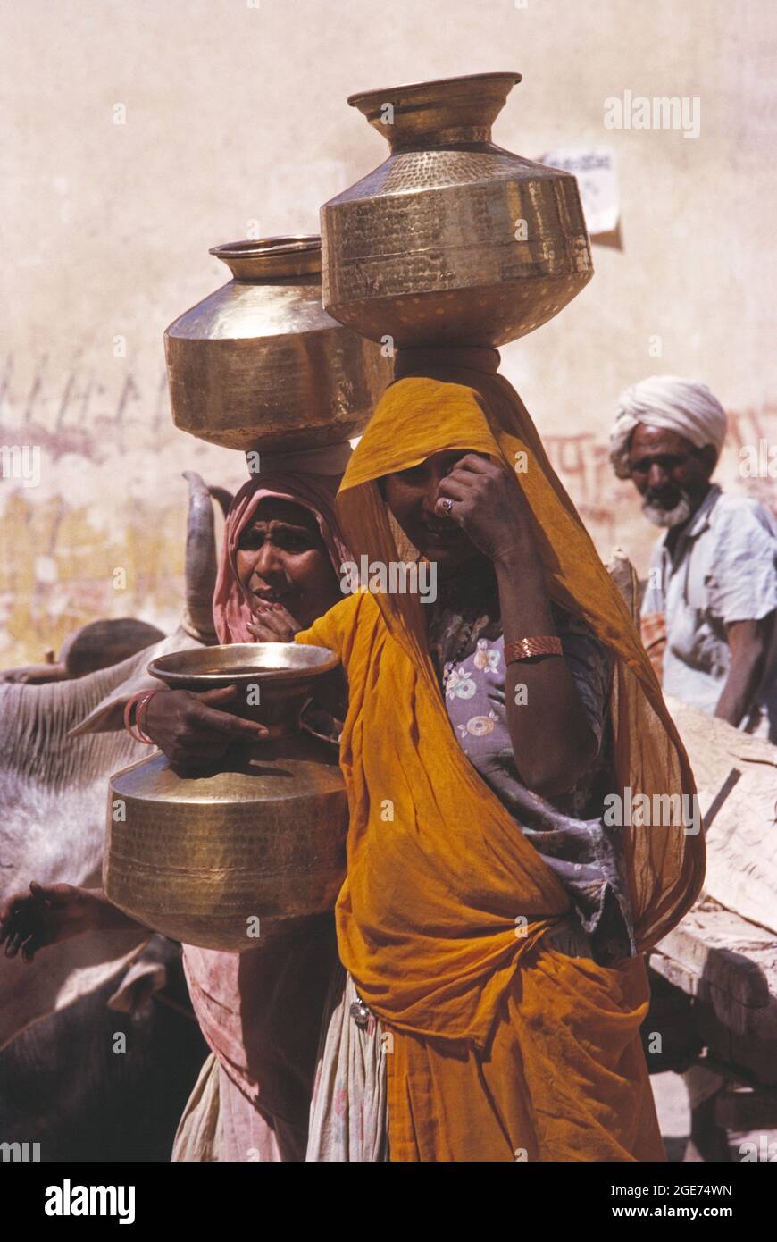 India. Rajasthan. Bundi. Donne locali che trasportano vasi d'acqua di ottone sulle loro teste. Foto Stock