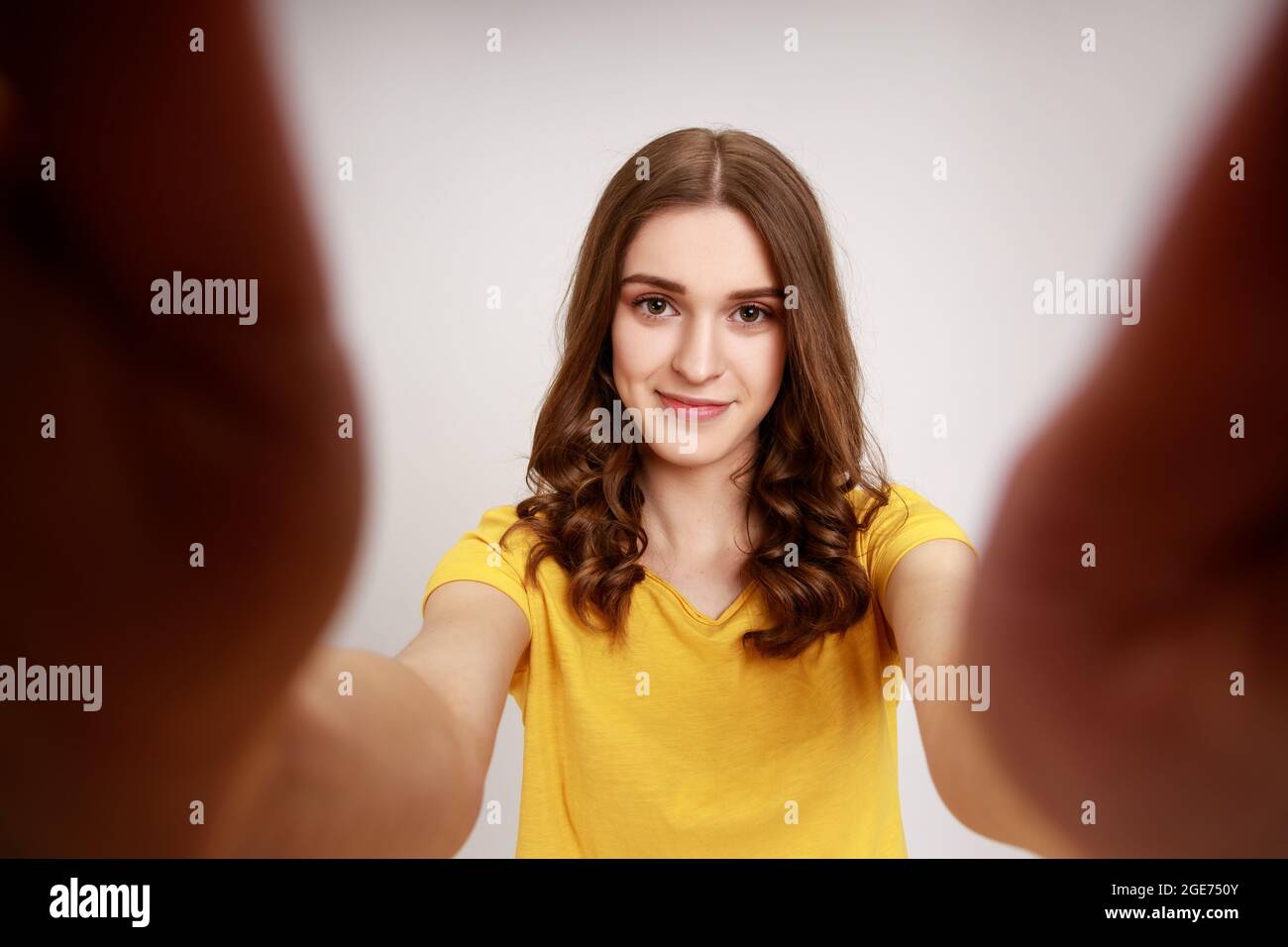 Ritratto di bella ragazza teenager piacevole aspetto in giallo casual T-shirt presa selfie, guardando la fotocamera con emozione positiva POV. studi interni Foto Stock