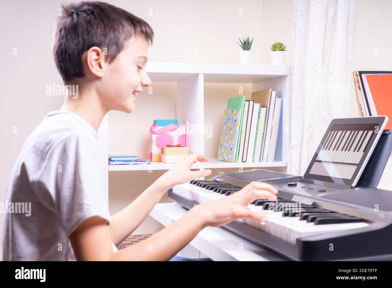 Ragazzo che guarda la video lezione al computer tablet e si diverte a  suonare il pianoforte a casa. Formazione online in remoto Foto stock - Alamy
