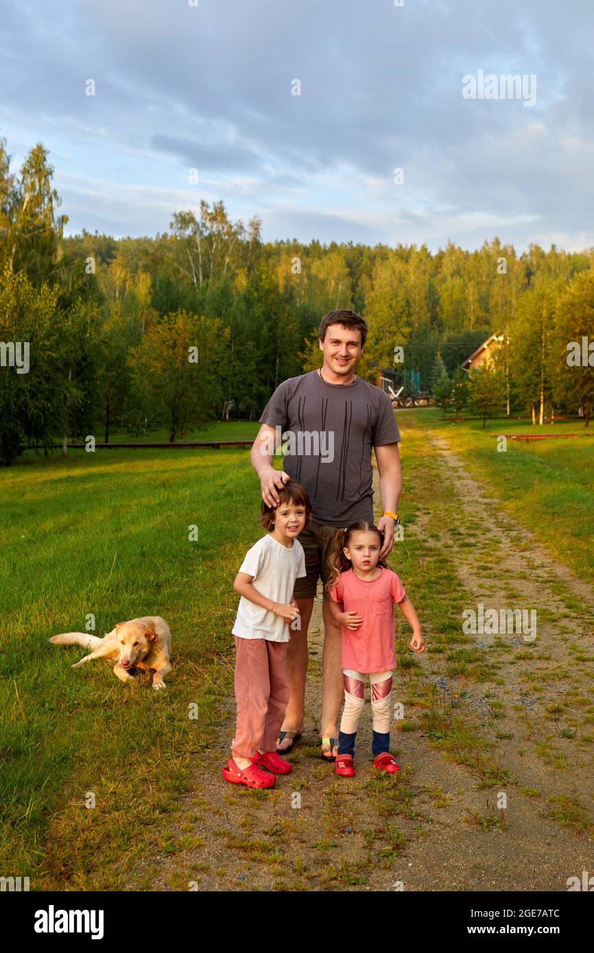 Uomo adulto con figlia e figlio in piedi sul percorso vicino cane fedele il giorno del fine settimana estivo in natura Foto Stock