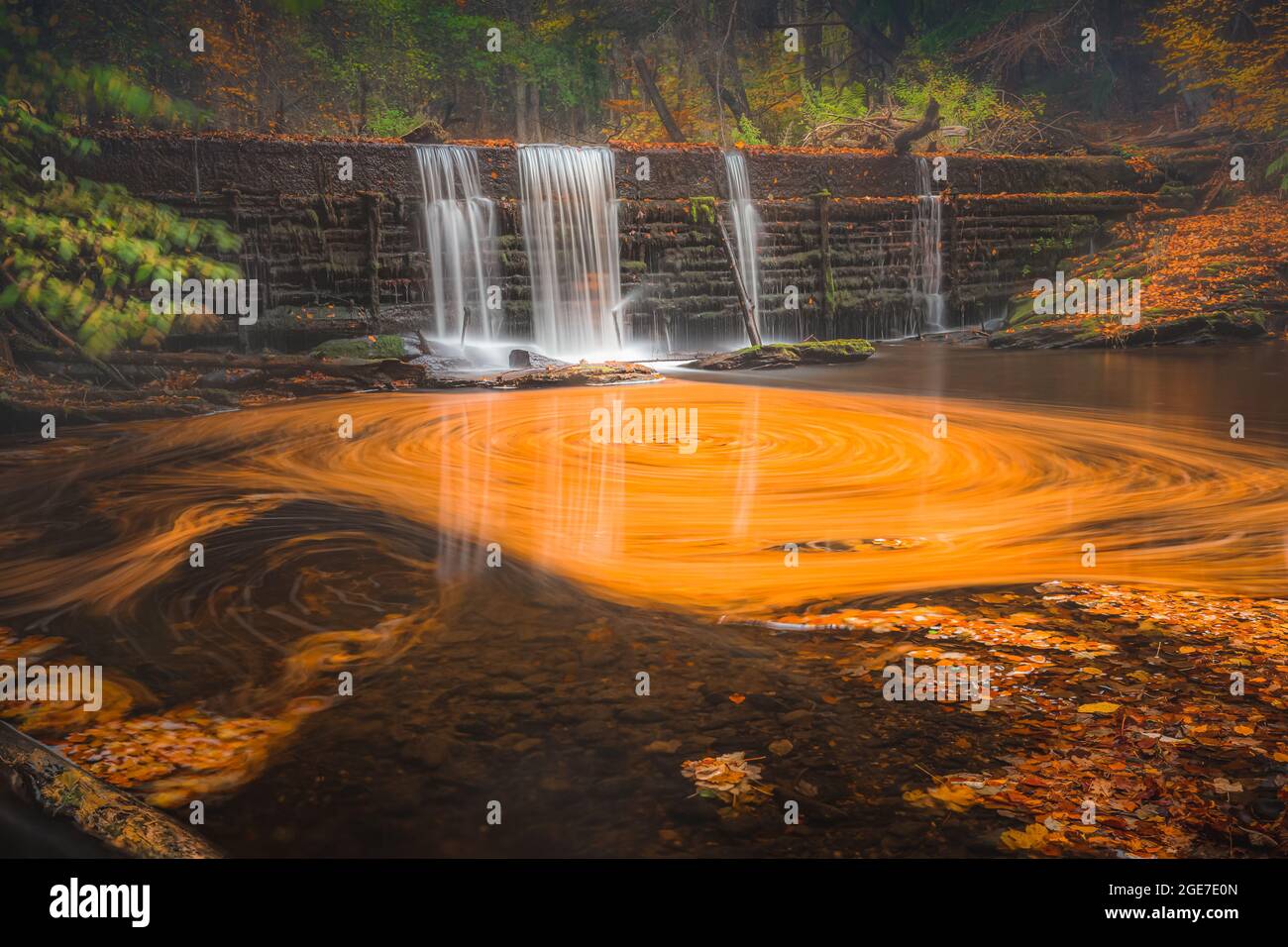 Una lunga esposizione di una cascata fa roteazioni di foglie autunnali che assomiglia ad una pittura arancione in un'intima scena boschiva a Gore Glen vicino Edinburgh, SC Foto Stock