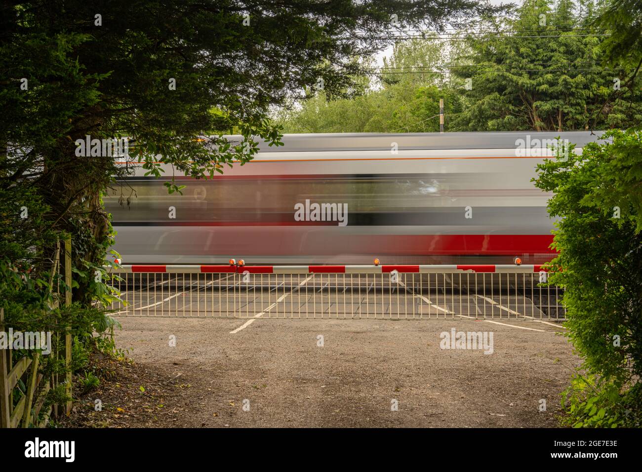 Treno offuscato che passa attraverso l'attraversamento a livello con barriere verso il basso vicino Margaretting Essex Foto Stock