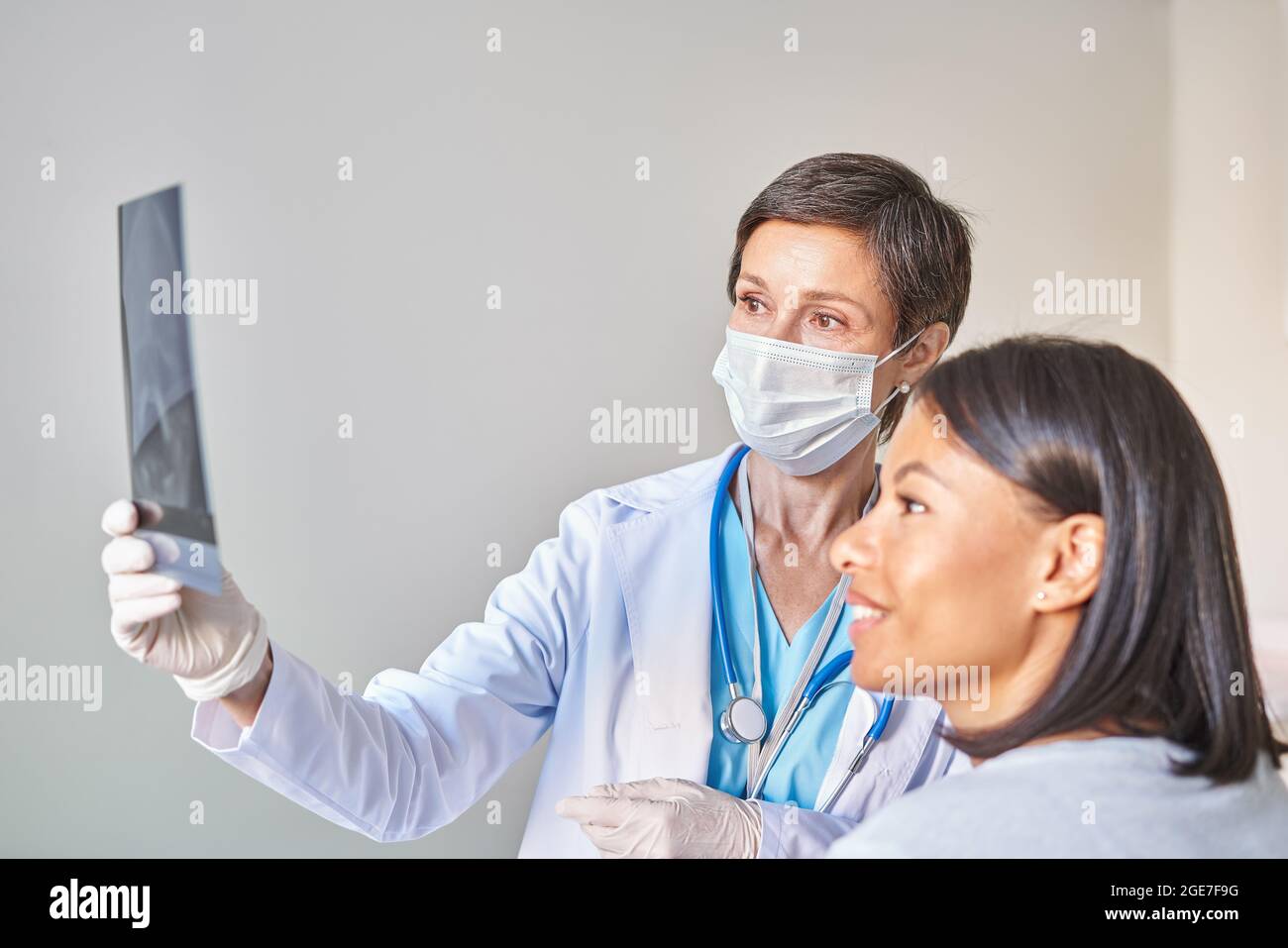 Medico femminile maturo in maschera medica di faccia che discute il risultato della risonanza magnetica con la donna africana sorridente Foto Stock