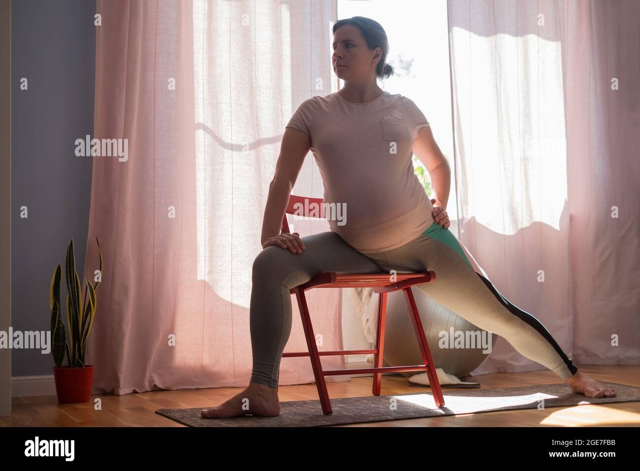 Yoga prenatale a casa. Donna incinta di lunghezza intera che fa l'esercitazione di yoga che allunga le gambe. Foto Stock