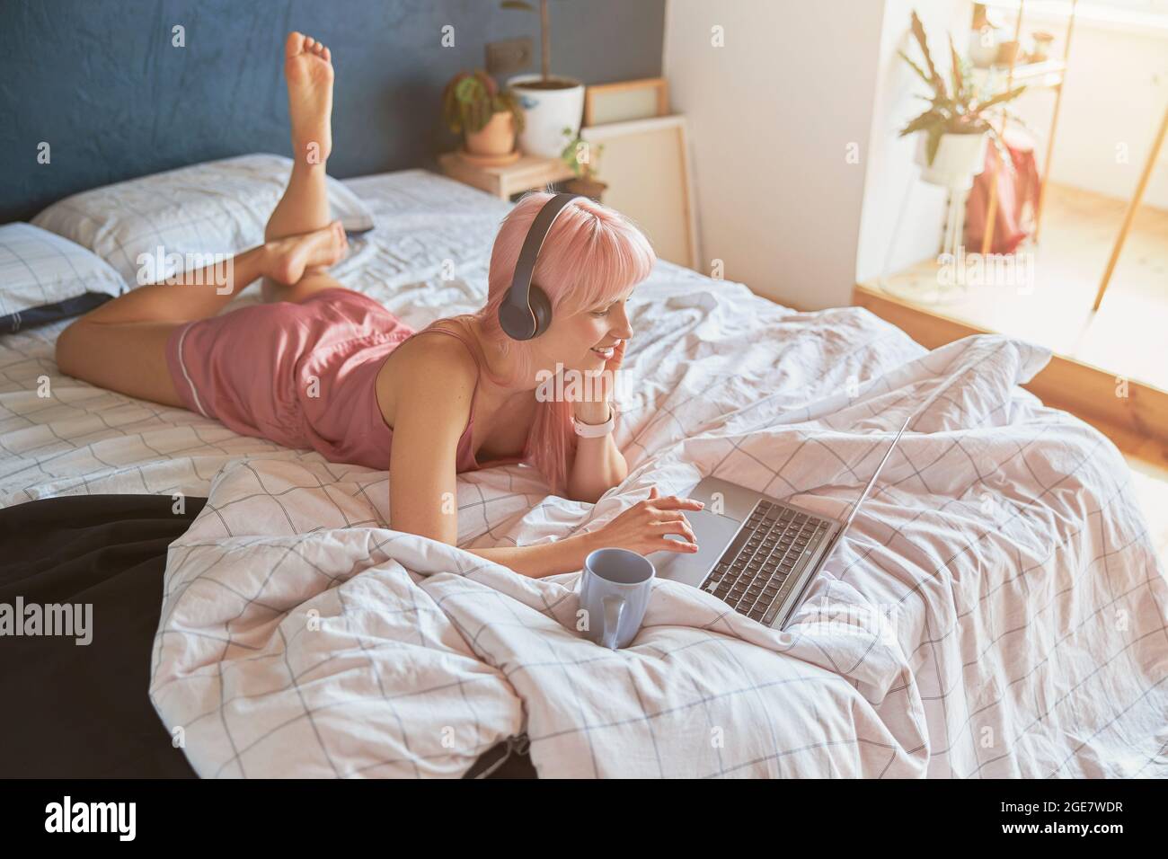 Bella donna con cuffie surfs internet con computer portatile sdraiato a letto al mattino Foto Stock