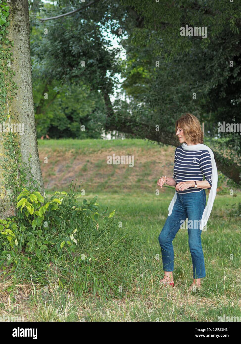 Donna anziana caucasica che indossa una camicia a righe e pantaloni in  denim in un parco Foto stock - Alamy