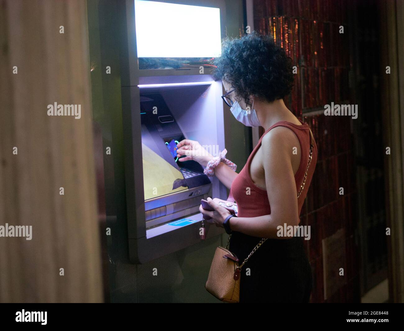 Una giovane donna ritira denaro da una macchina ATM di notte Foto Stock