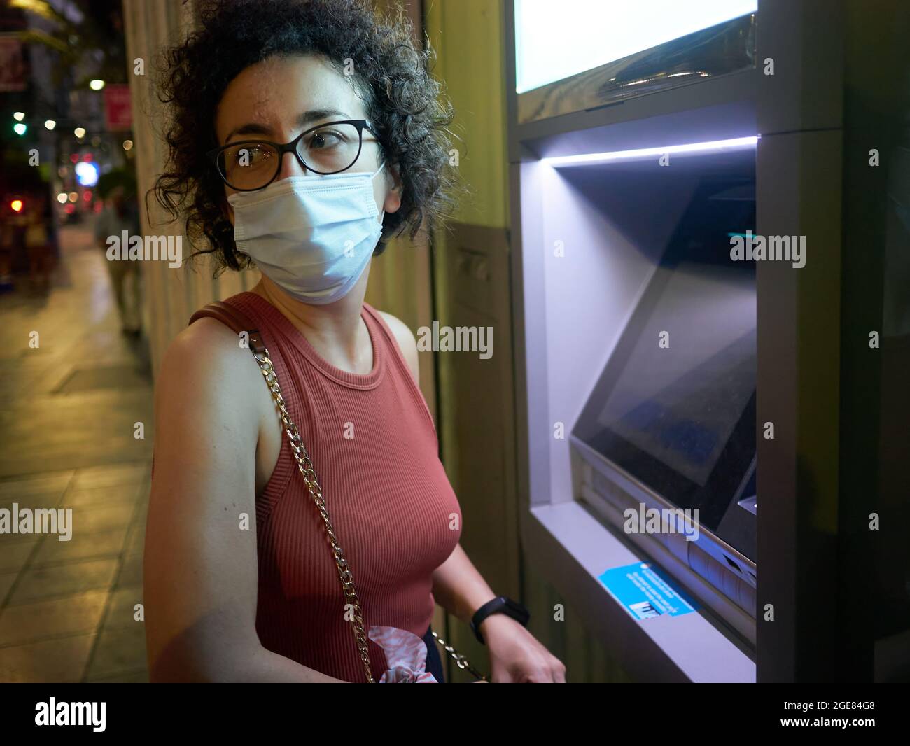 Una giovane donna ritira denaro da una macchina ATM di notte Foto Stock