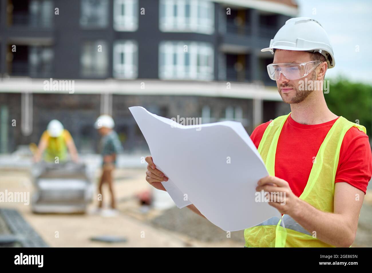 Ingegnere in un gilet e un elmetto che studia un piano di costruzione Foto Stock