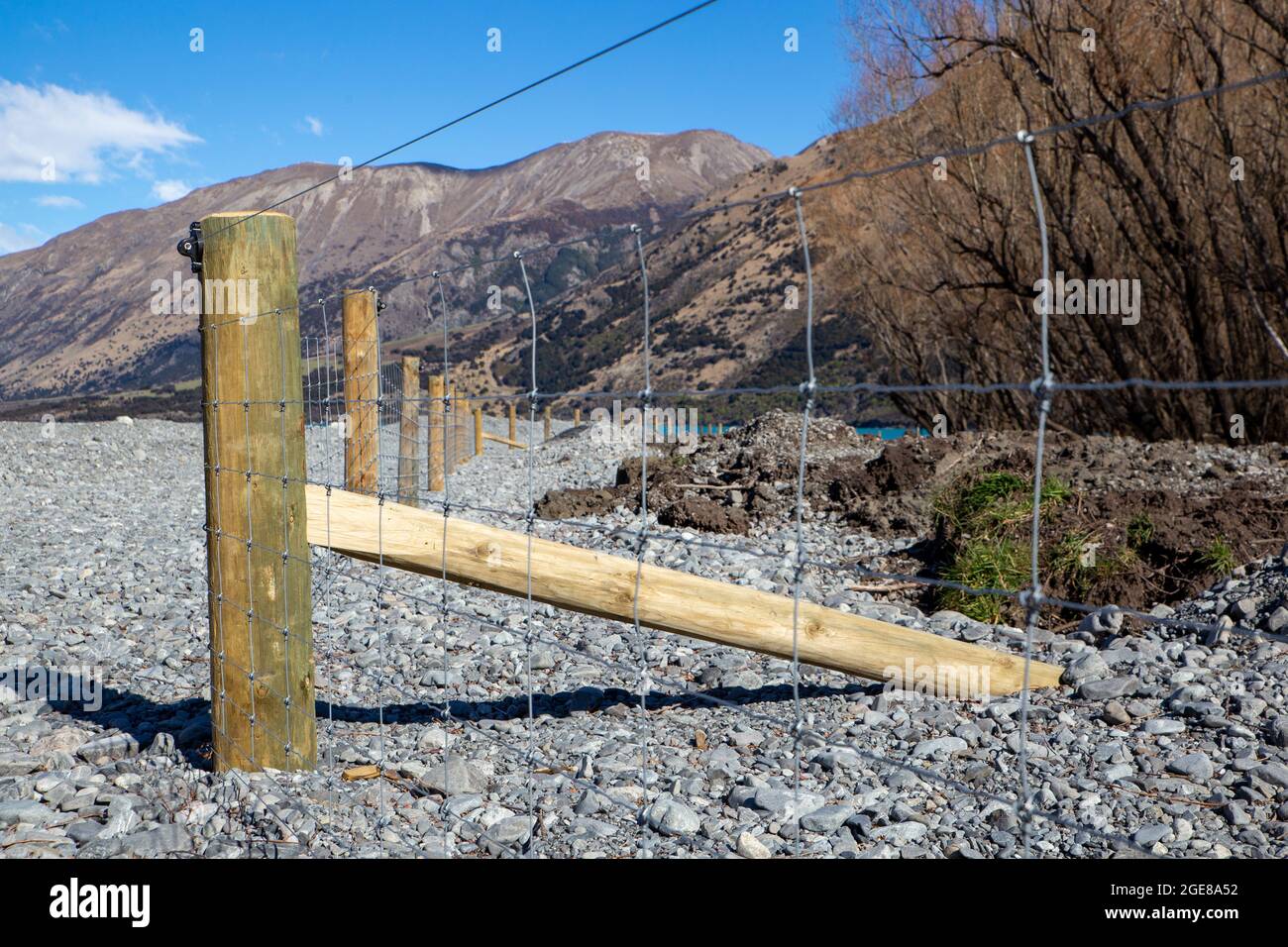 Nuovo palo e recinzione di rete che divide il confine della fattoria dal letto del fiume nel paese alto, Canterbury, Nuova Zelanda Foto Stock